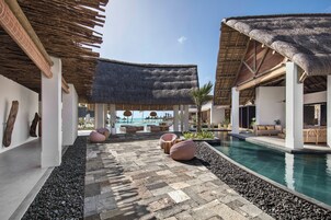 Un área de piscina en un complejo turístico con estructuras de techo de paja, asientos y una vista despejada del océano.