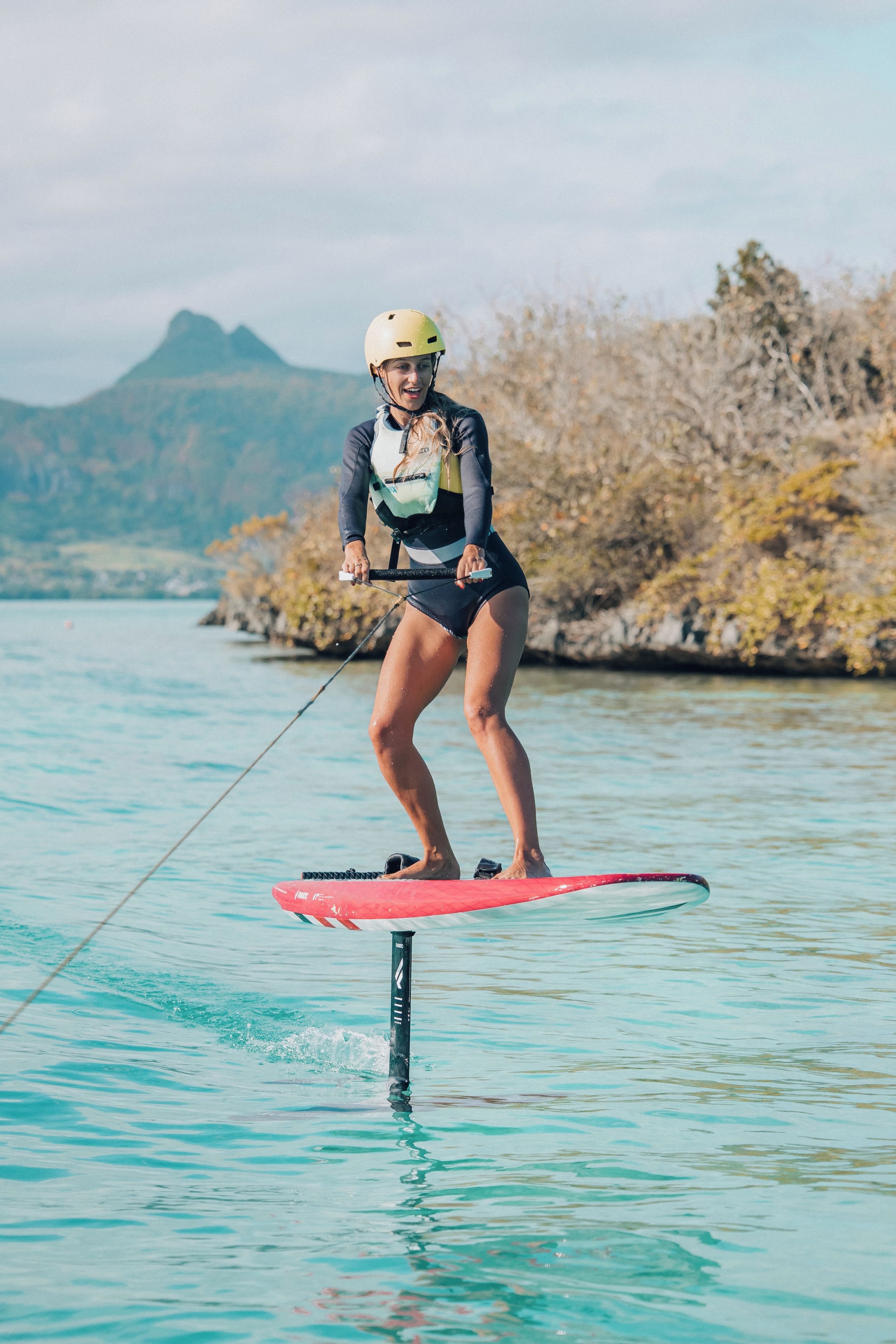 Eine Person beim Wakeboarden auf einem Gewässer, im Hintergrund eine gebirgige Landschaft.