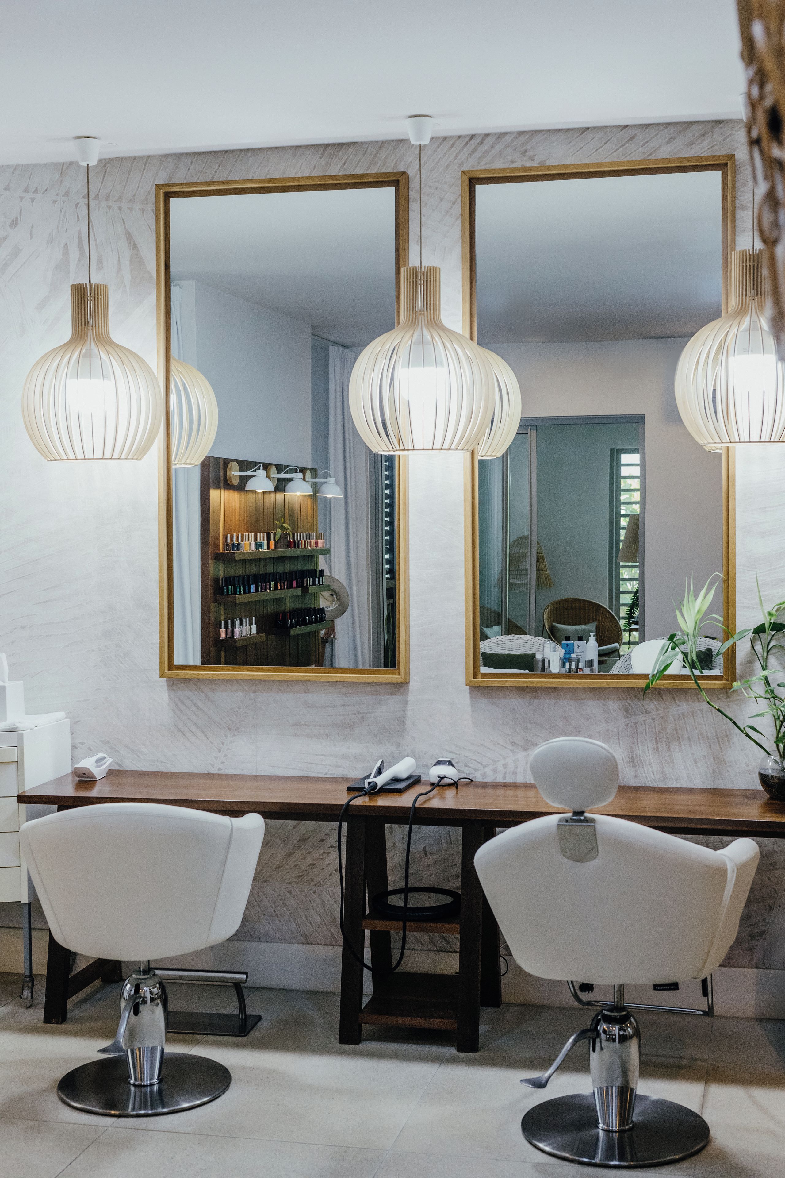 A modern salon with two white chairs, a wooden desk, and three pendant lights.