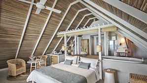 A spacious attic bedroom with a large bed, two wicker chairs, a small table, and a built-in bathtub.