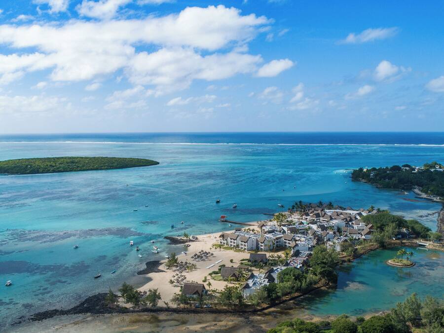Ein Luftbild eines Küstenresorts mit Strand, klarem türkisfarbenem Wasser und einer kleinen Insel.