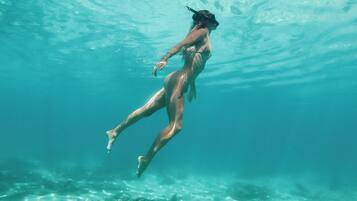 A person swimming underwater with clear water and a rocky bottom.