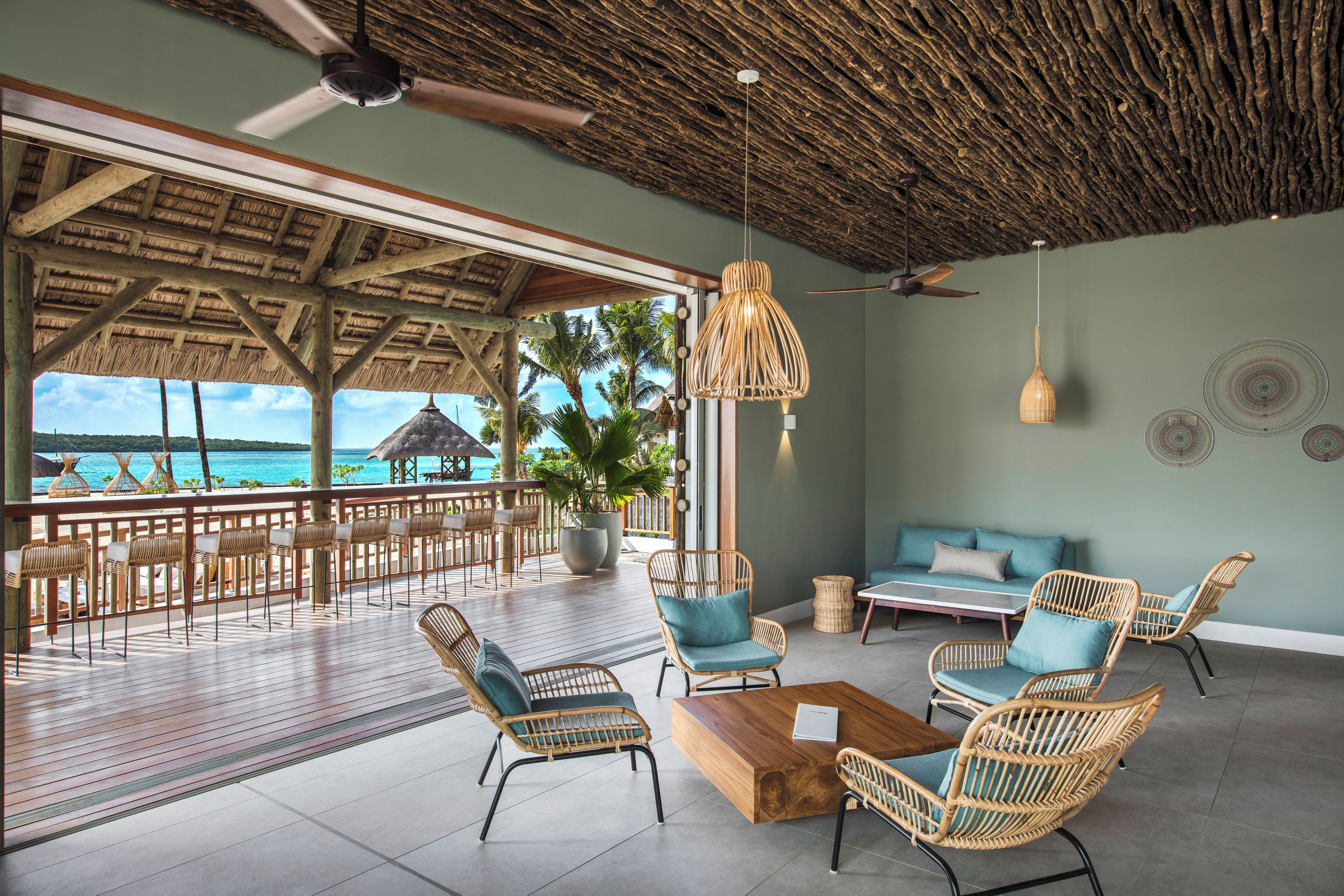 A spacious outdoor seating area with wicker furniture, a wooden coffee table, and a view of the ocean.
