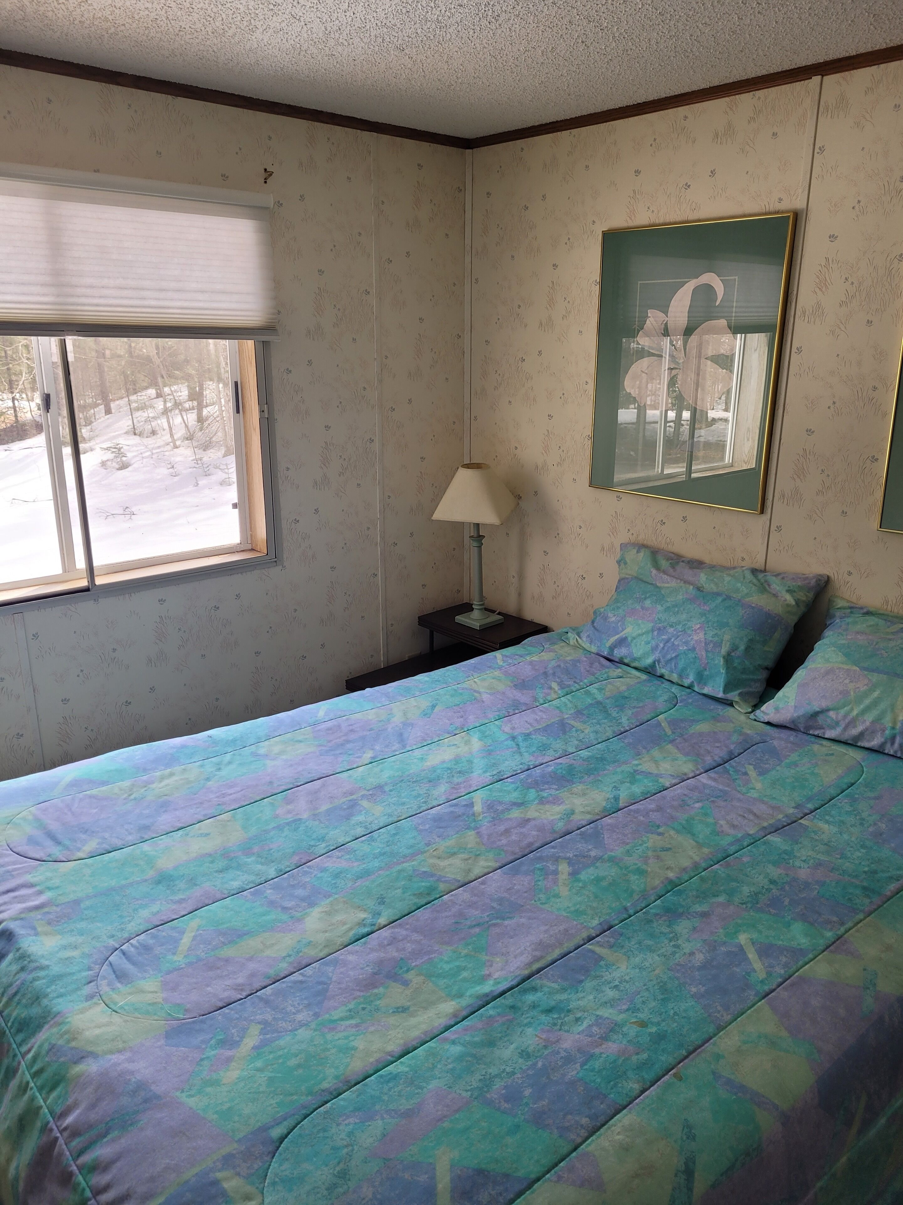 A bedroom with a bed, a nightstand, a lamp, a window, and a framed picture on the wall.