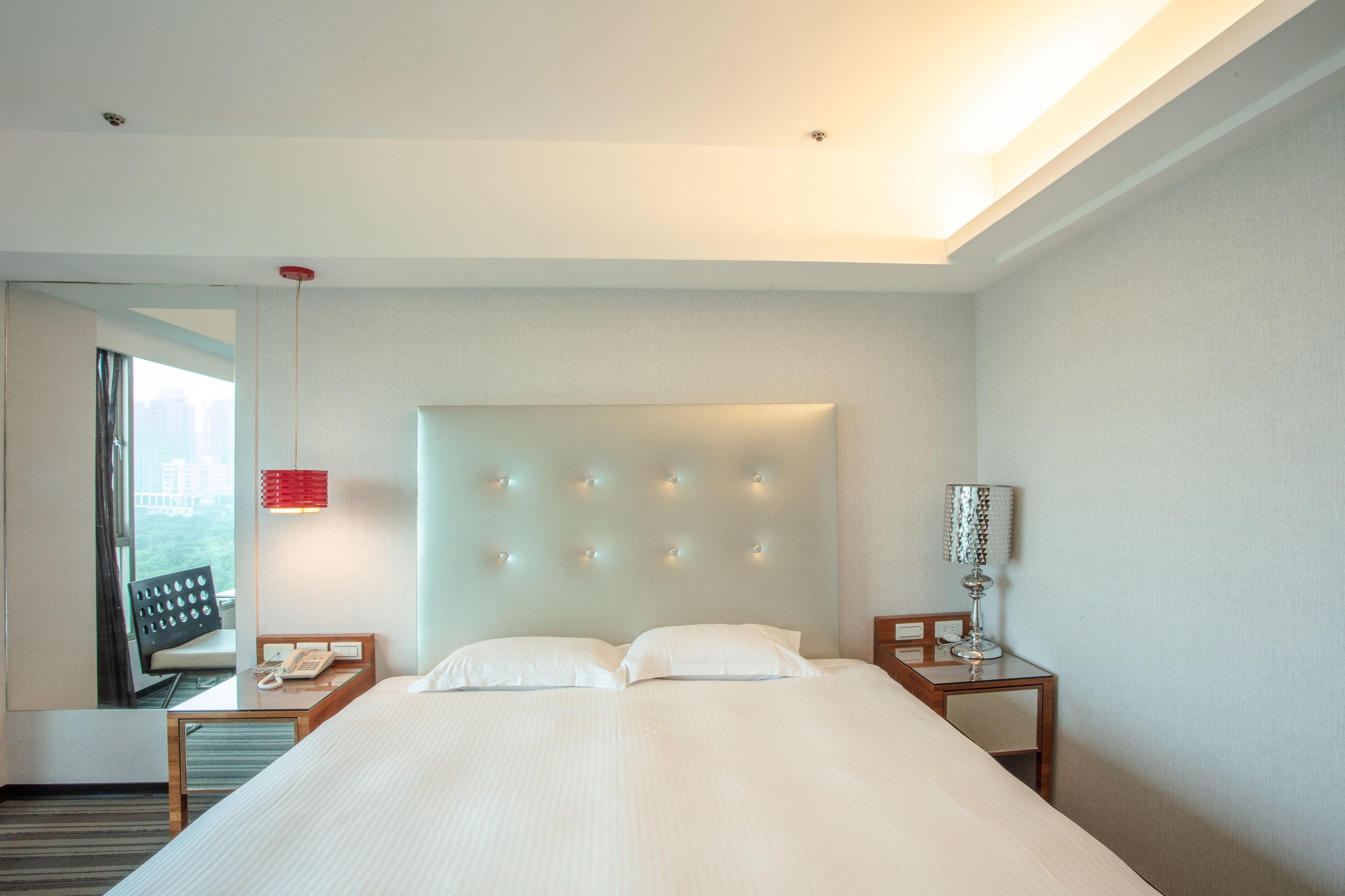 A hotel room with a large bed, a bedside table with a lamp, and a window with curtains.