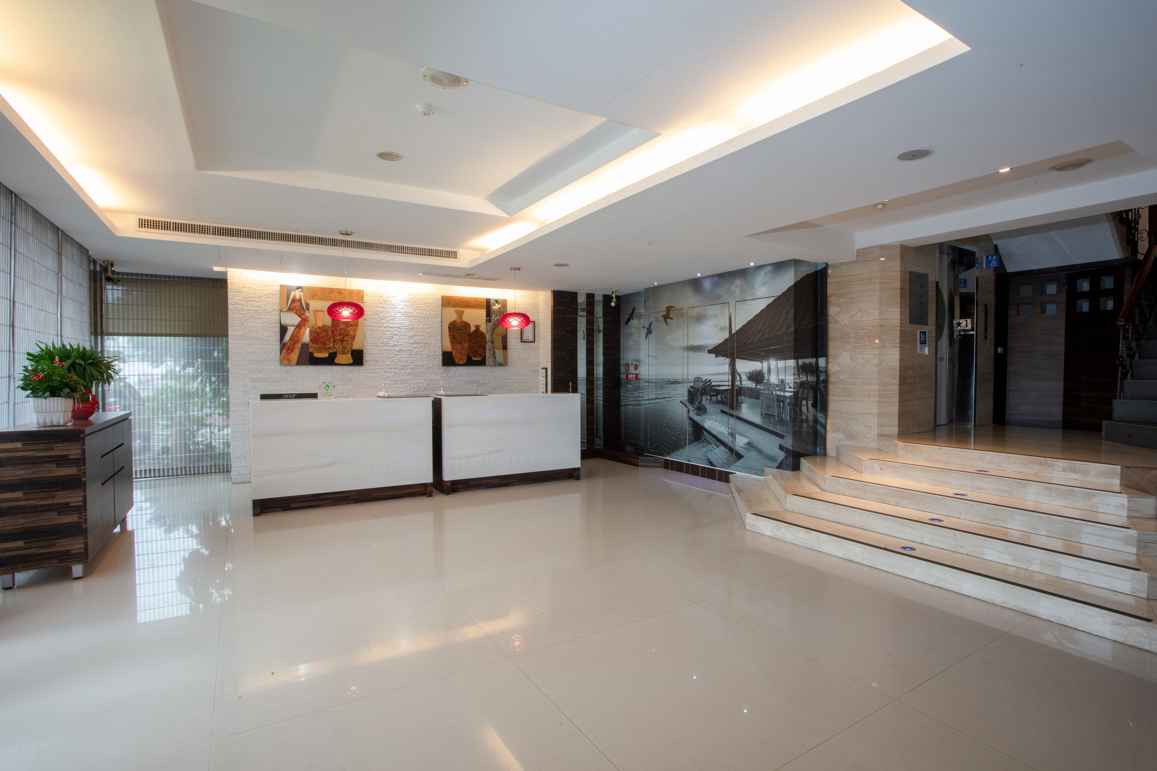 A modern reception area with a white reception desk, a large abstract mural, and a staircase leading to an upper level.