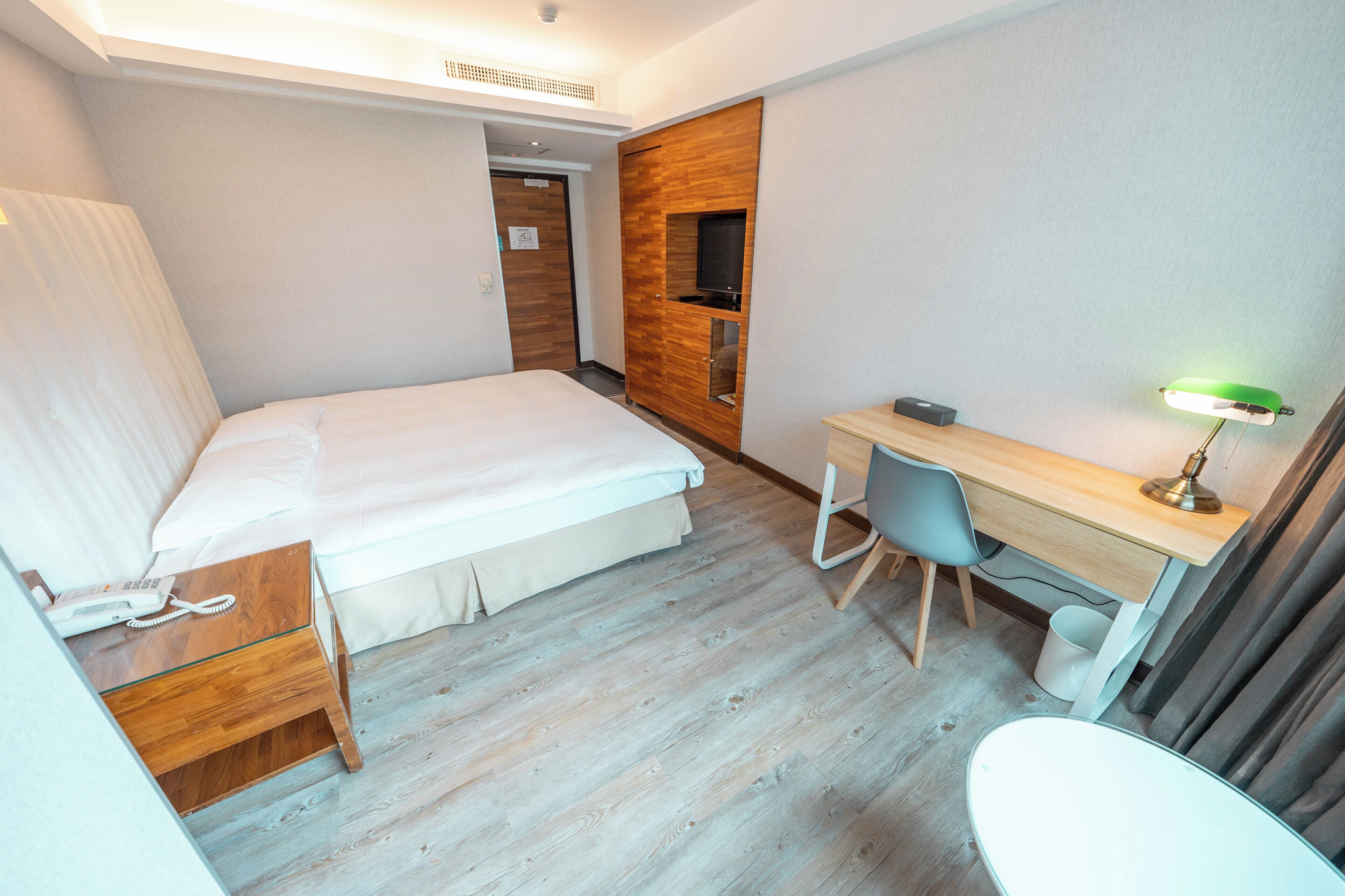 Ein Hotelzimmer mit einem Bett, einem Schreibtisch mit Stuhl, einem Telefon und einem Fernseher.