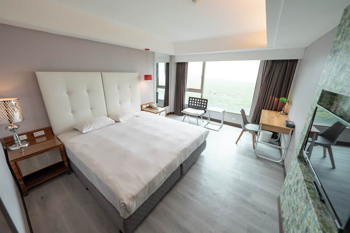Habitación de hotel con una cama grande, un escritorio, una silla, una mesita y vistas al exterior.