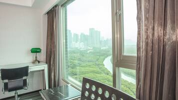 A room with a desk, chair, and a large window offering a view of a river and greenery.