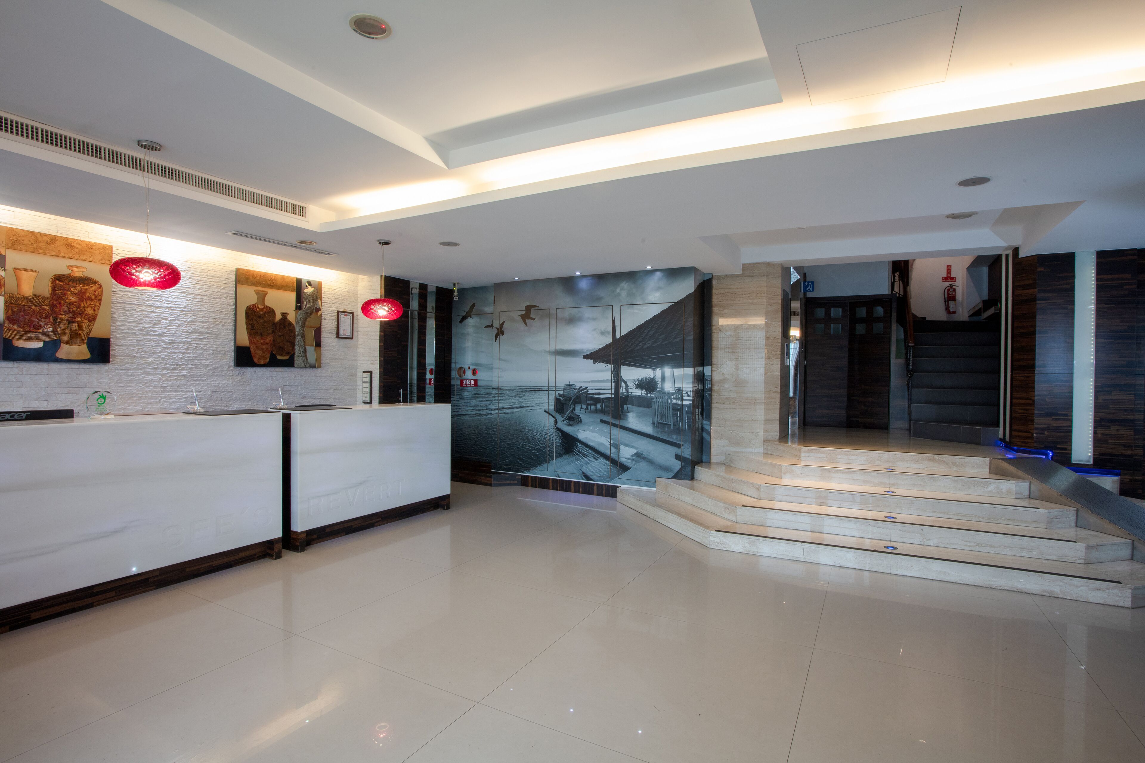 A modern reception area with a white reception desk, a mural of birds and a boat, and a staircase leading to an upper level.