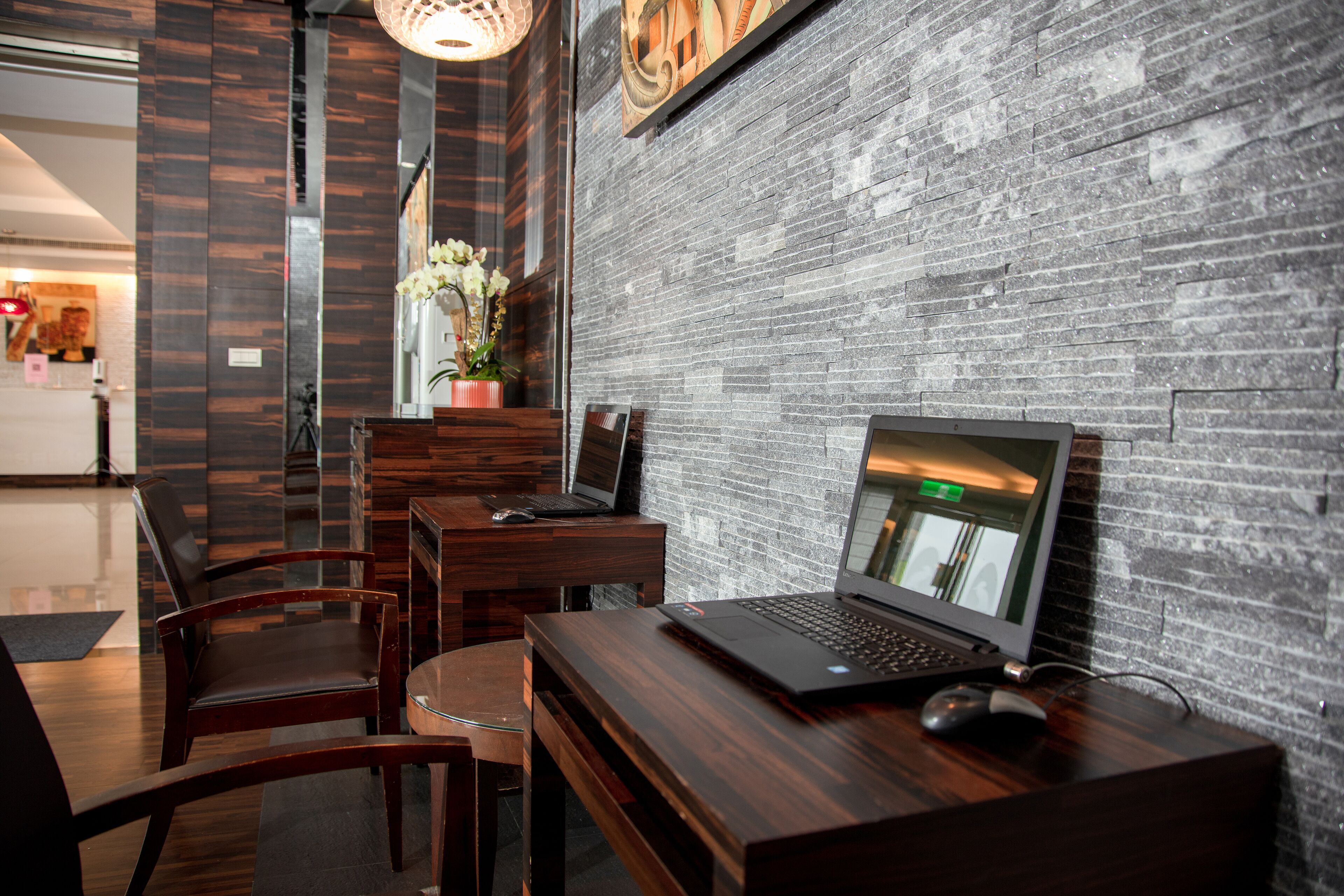 A modern hotel lobby with a brick wall, wooden furniture, and a laptop on a desk.