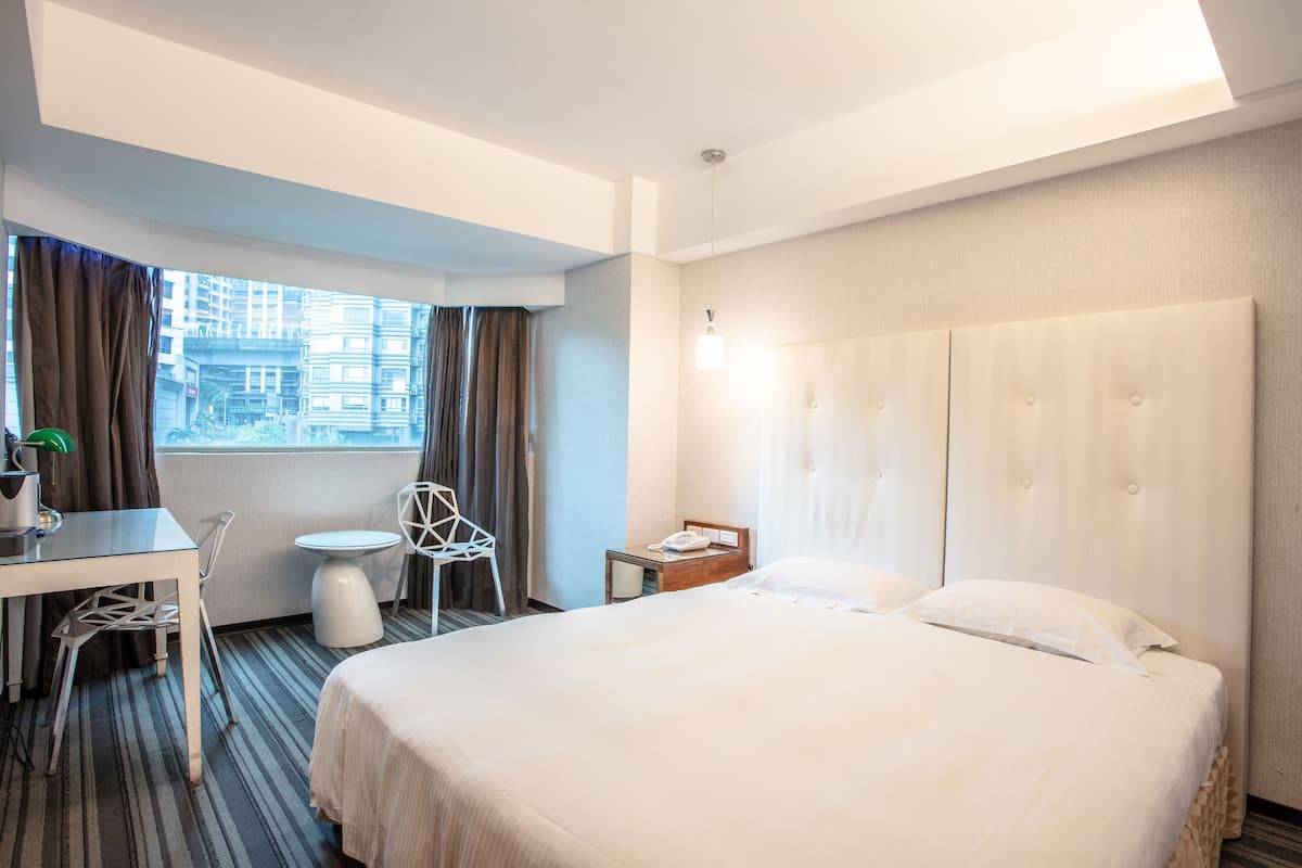 Una habitación de hotel con cama, escritorio, silla, mesita y ventana con cortinas.
