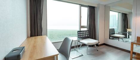 Una habitación de hotel con un ventanal grande, un escritorio de madera, una silla y un espejo.