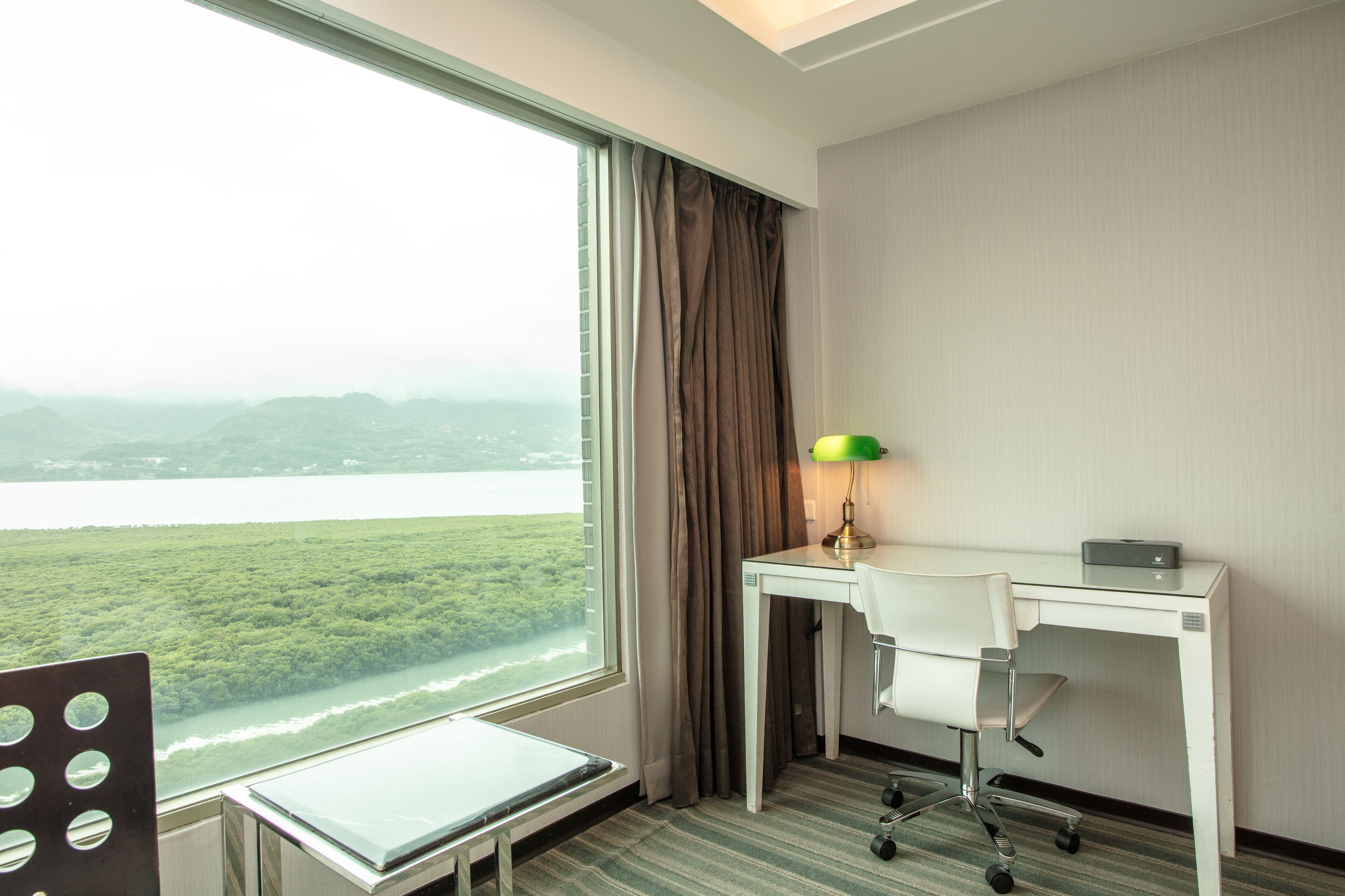 A hotel room with a desk, chair, and a view of a river and mountains.