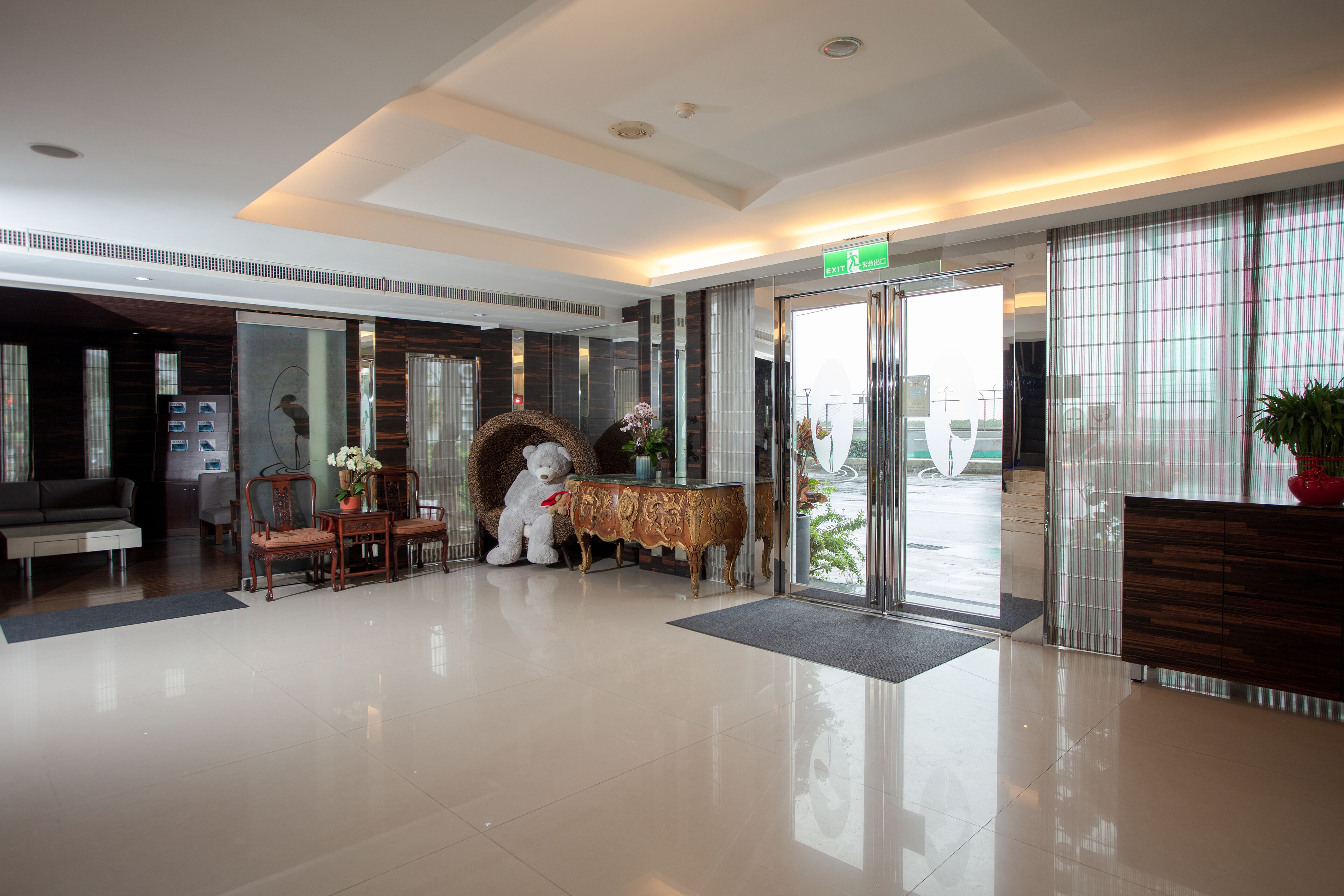 A hotel lobby with a reception desk, a sofa, chairs, a decorative wall, and a large window.