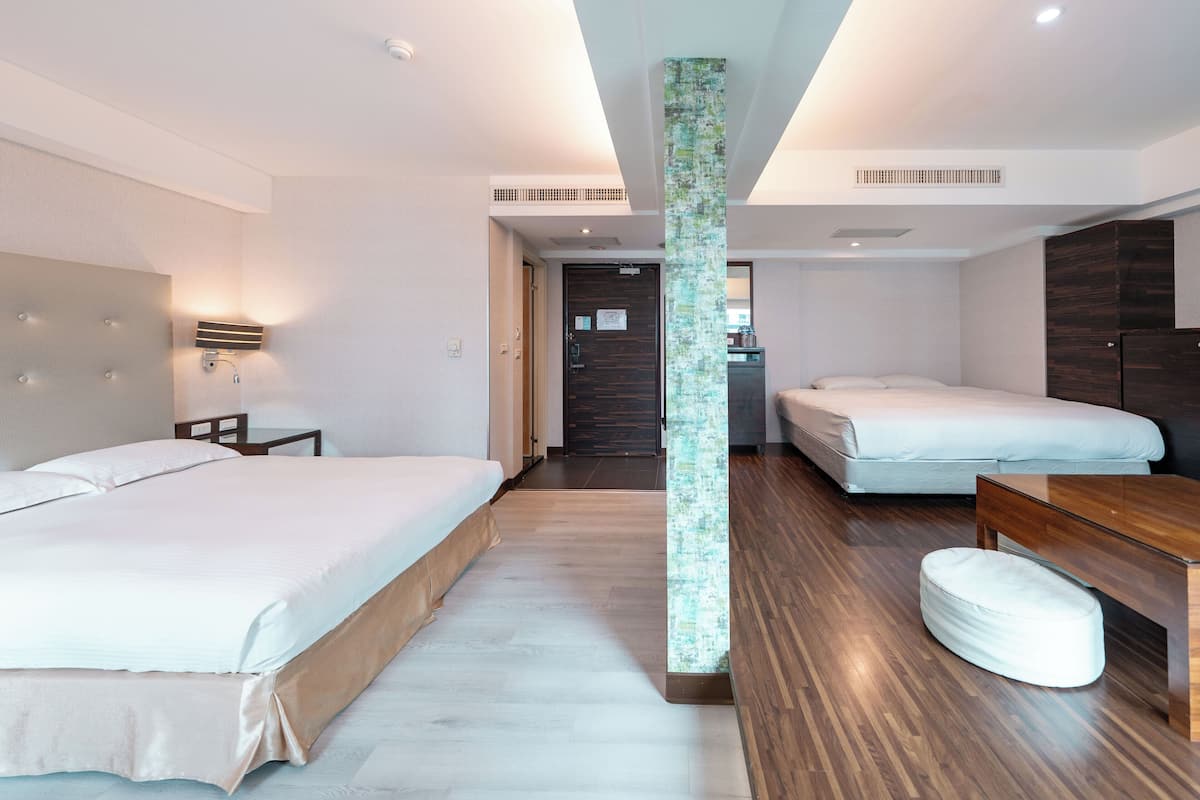 Habitación de hotel con dos camas, suelo de madera, un pilar central y un pequeño rincón de descanso.