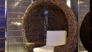 A modern, spherical chair with a unique woven pattern, placed in a contemporary room with dark wood paneling and a reflective floor. - Hotel Cloud Riverside (New Taipei City)