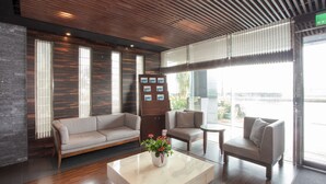 A modern lobby with a sofa, armchairs, a coffee table with a flower vase, wooden panel walls, and large windows. - Hotel Cloud Riverside (New Taipei City)