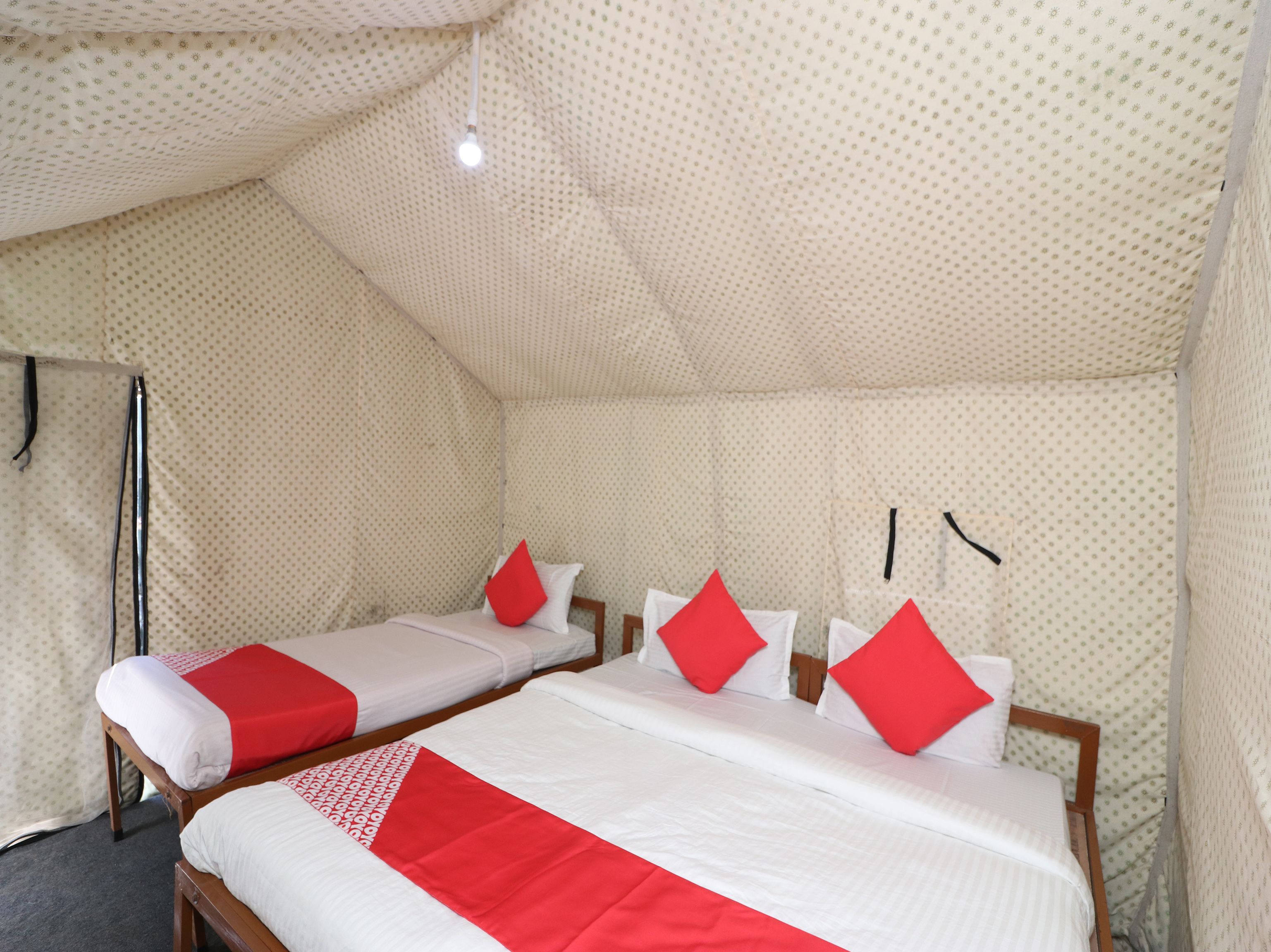 A room with two beds, each with white bedding and red accents, and a patterned ceiling.