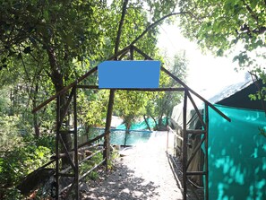 A wooden bridge with a blue sign, surrounded by trees and a body of water.