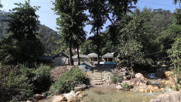 A natural setting with a clear stream, rocky terrain, and several tents with canopies. - OYO 23439 Tapovan Heights Camp & Resort (Narendranagar)