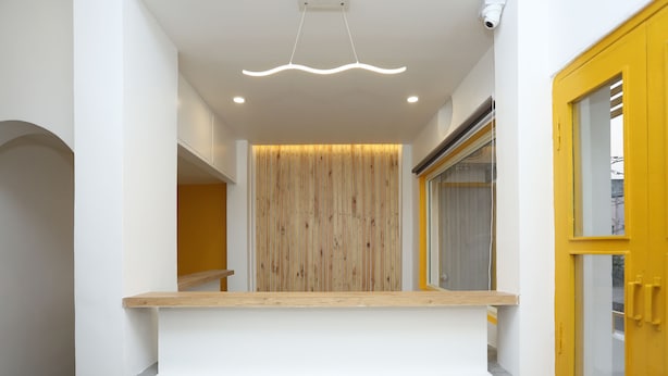Un espace d’accueil avec un mur recouvert de panneaux en bois, un comptoir en béton et une porte jaune.