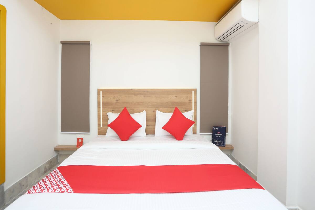 Habitación de hotel con una cama, almohadas rojas, un cabecero de madera y un equipo de aire acondicionado.