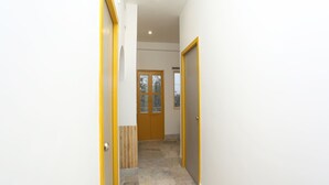 Un couloir avec une porte en bois au fond, un sol carrelé et un mur blanc orné d’une bordure jaune.