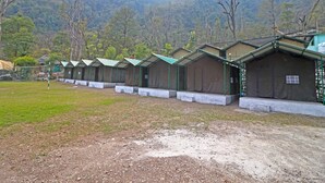 A row of simple, single-story cabins with green roofs, set against a backdrop of a forested hillside. - OYO 29047 Yoyo Moonlight (Narendranagar)