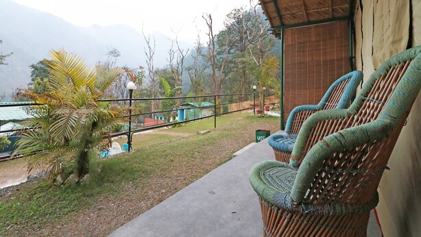 A balcony with wicker chairs, a view of mountains, and a thatched roof structure. - OYO 29047 Yoyo Moonlight (Narendranagar)