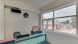 A reception desk with a clock, a security camera, and a window with a view of buildings and palm trees. - OYO Flagship 29620 New Champion Residency (Bengaluru)