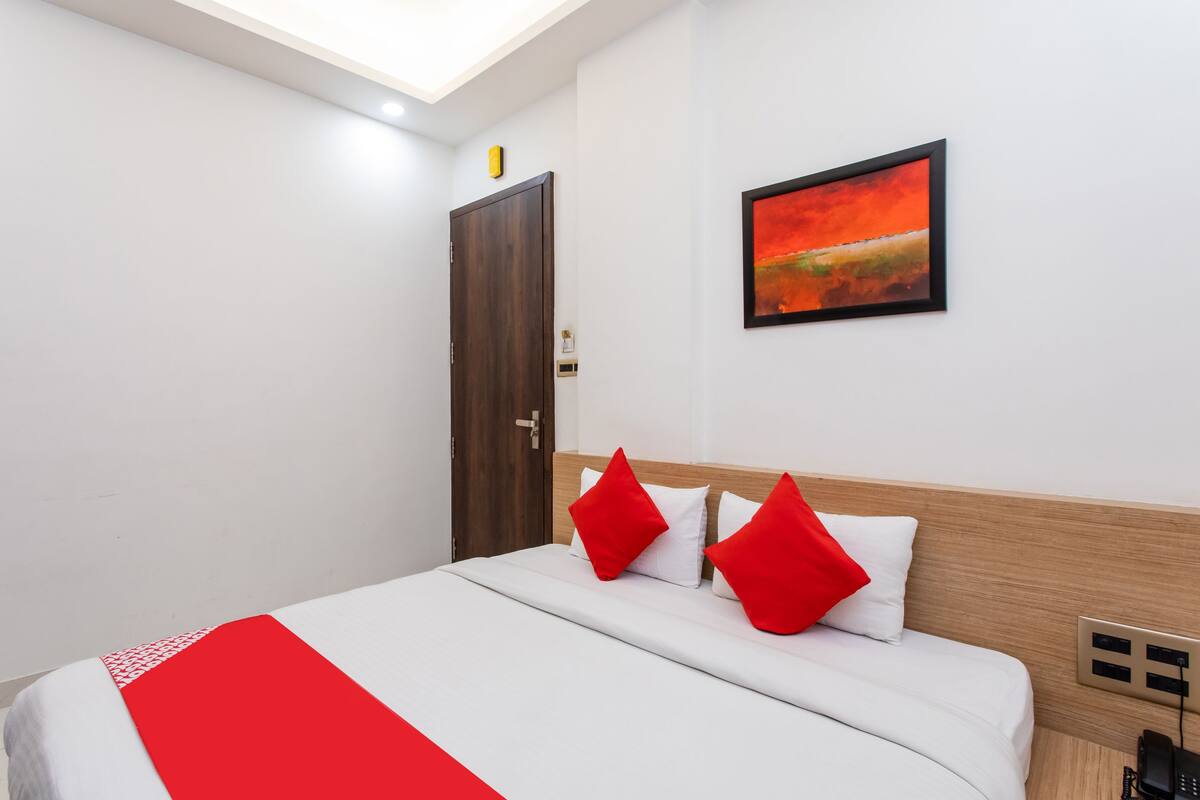 Ein Hotelzimmer mit einem Bett, einem Gemälde an der Wand, einer Holztür und einer Steckdose.