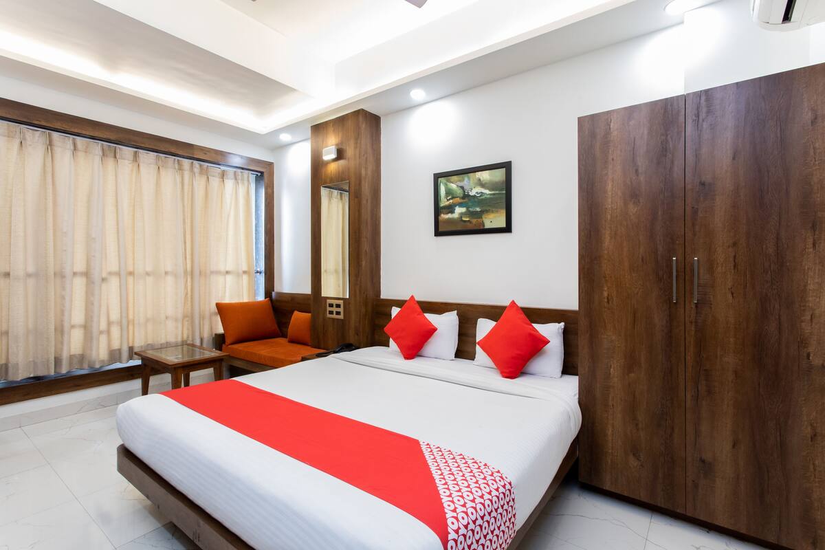 Ein Hotelzimmer mit einem großen Bett, einem Holzschrank, einem kleinen Tisch und einem Fenster mit Vorhängen.