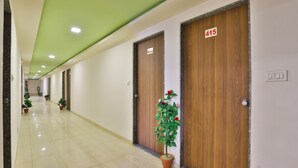 A hallway with wooden doors numbered 414 and 415, potted plants, and a green ceiling. - Hotel Tirupati - Ahmedabad (Ahmedabad)