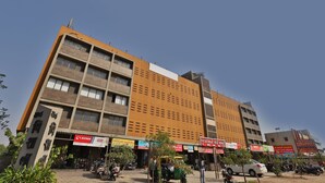 A multi-story building with various shops on the ground floor, including a visible sign for 'Eicher'. - Hotel Tirupati - Ahmedabad (Ahmedabad)