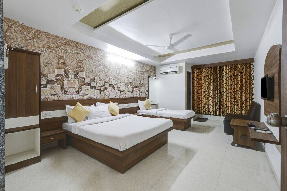 A hotel room with a large bed, a desk, a chair, an air conditioning unit, and a television.