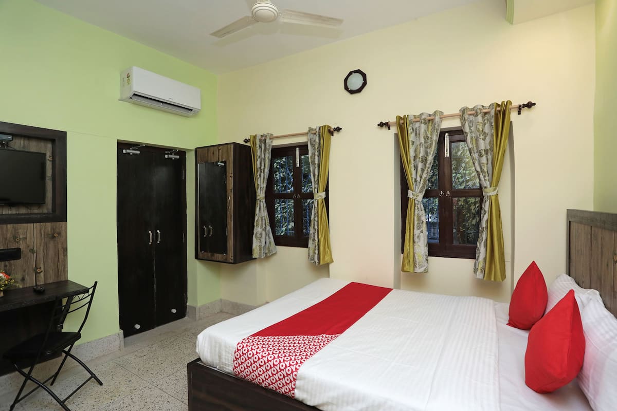 A bedroom with a bed, two windows with curtains, a ceiling fan, and an air conditioning unit.