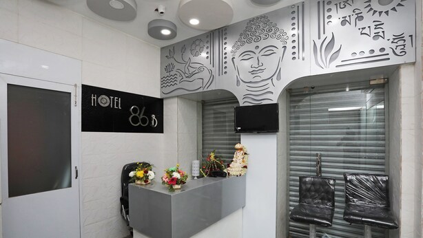 Zona de recepción de un hotel con diseño moderno, que incluye un mostrador, una silla, un televisor y una pared decorativa.