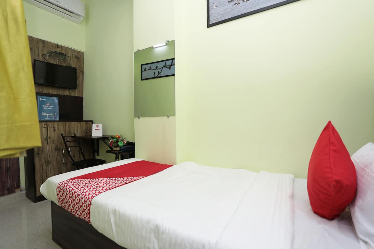A hotel room with a bed, a desk, a chair, a TV mounted on the wall, and a sign on the wall.