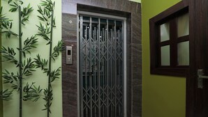 Una habitación con una reja metálica, un interruptor de luz instalado en la pared y una puerta de madera con un ventanal.