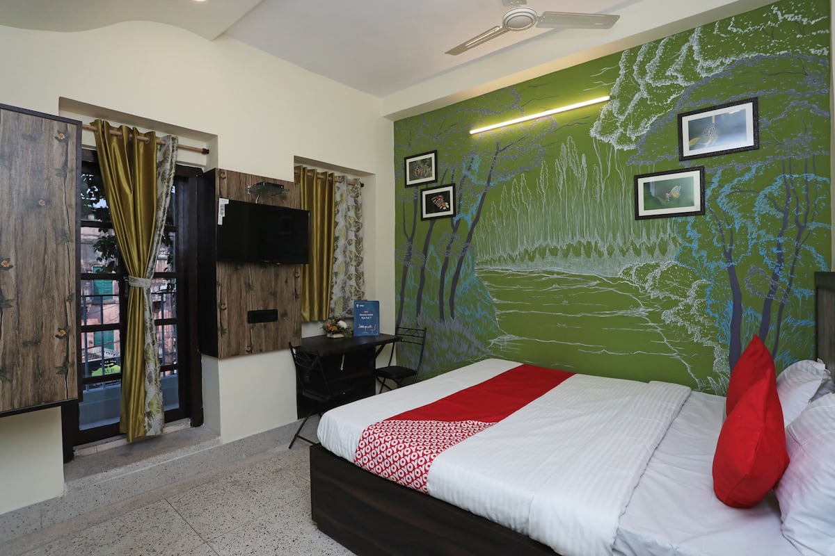 A bedroom with a bed, a desk, a chair, a TV, and a green mural on the wall.