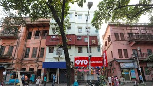 Hotel con un llamativo letrero rojo, un balcón y vistas a la calle con peatones y scooters estacionados.