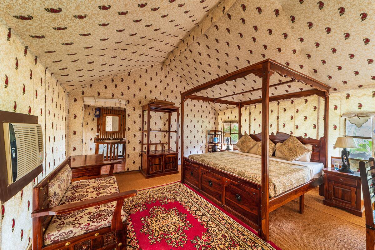 Ein Bett mit Baldachin, dessen Gestell aus Holz besteht, ein roher Teppich mit Muster und eine Tapete mit sich wiederholendem Design.