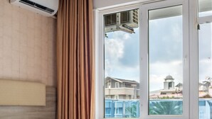 A hotel room with two beds, an air conditioning unit, a window with a view of buildings, and a curtain. - Ustun Apart Hotel (Alanya)