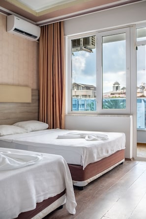 A hotel room with two beds, an air conditioning unit, a window with a view of buildings, and a curtain. - Ustun Apart Hotel (Alanya)
