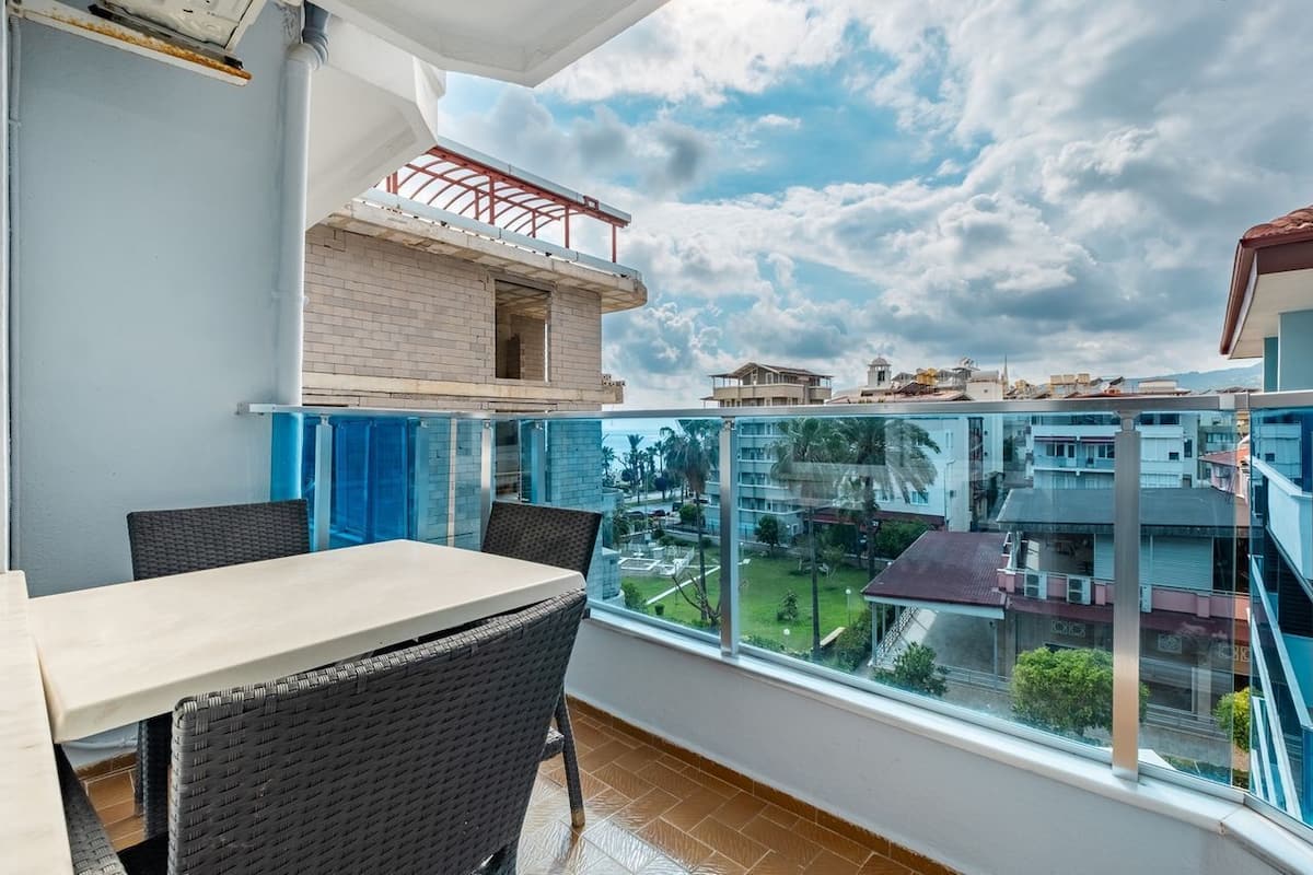 A balcony with a table and chairs, a view of the surrounding buildings, and a partially constructed structure.