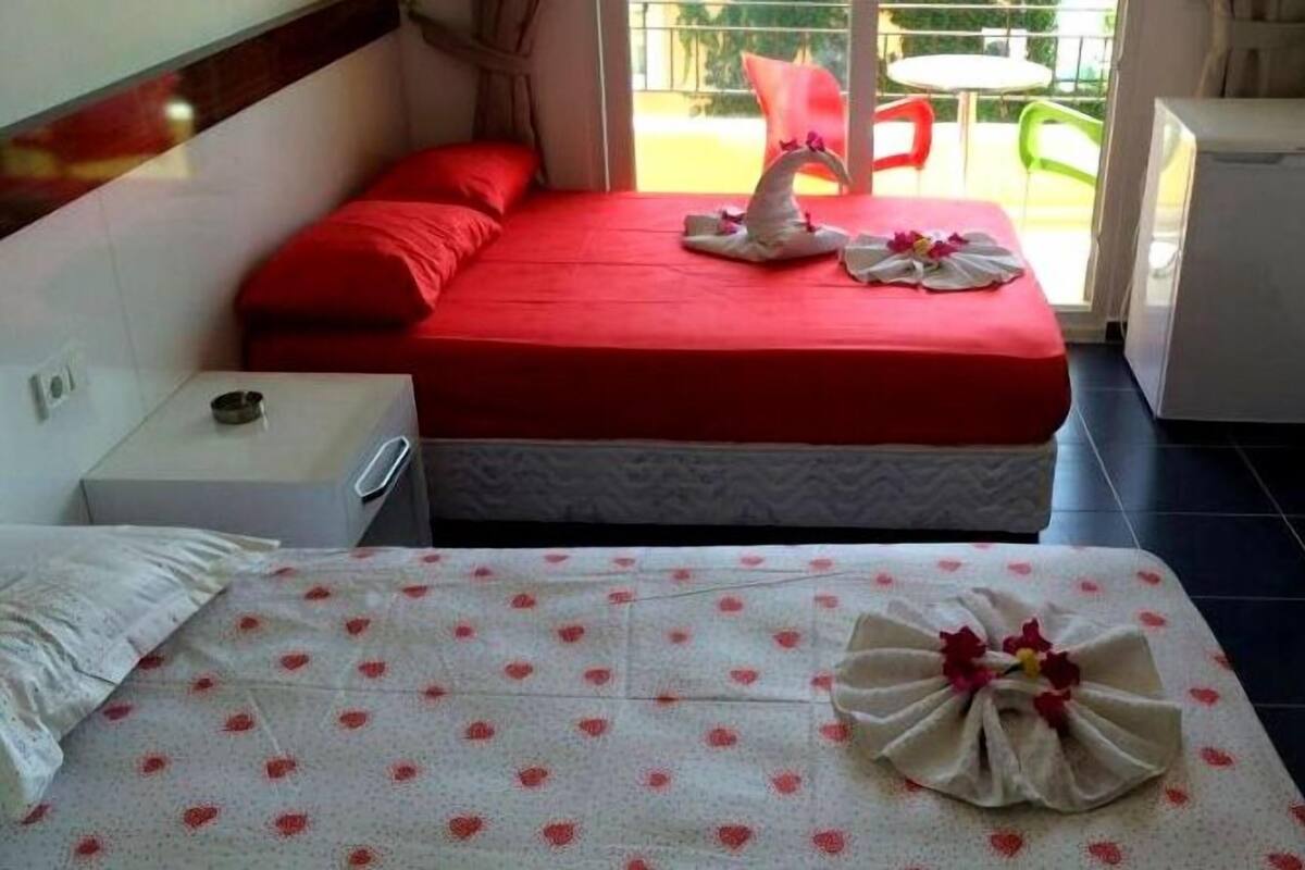 A hotel room with a bed, a bedside table, a small table with a chair, and a view of the outside.