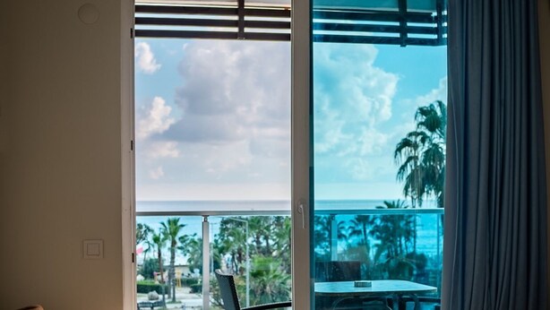 A room with a sofa, a dining table, and a view of the ocean through a sliding glass door. - Ustun Apart Hotel (Alanya)