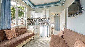 A compact living space with a kitchenette, two sofas, a TV, and a view through a window. - Ustun Apart Hotel (Alanya)