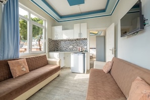 A compact living space with a kitchenette, two sofas, a TV, and a view through a window. - Ustun Apart Hotel (Alanya)